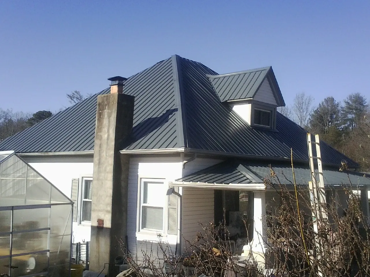 Dark blue standing seam metal roof on a white farmhouse with dormer — Slate & Tile Roof Repair by Roofing Brothers in Casar
