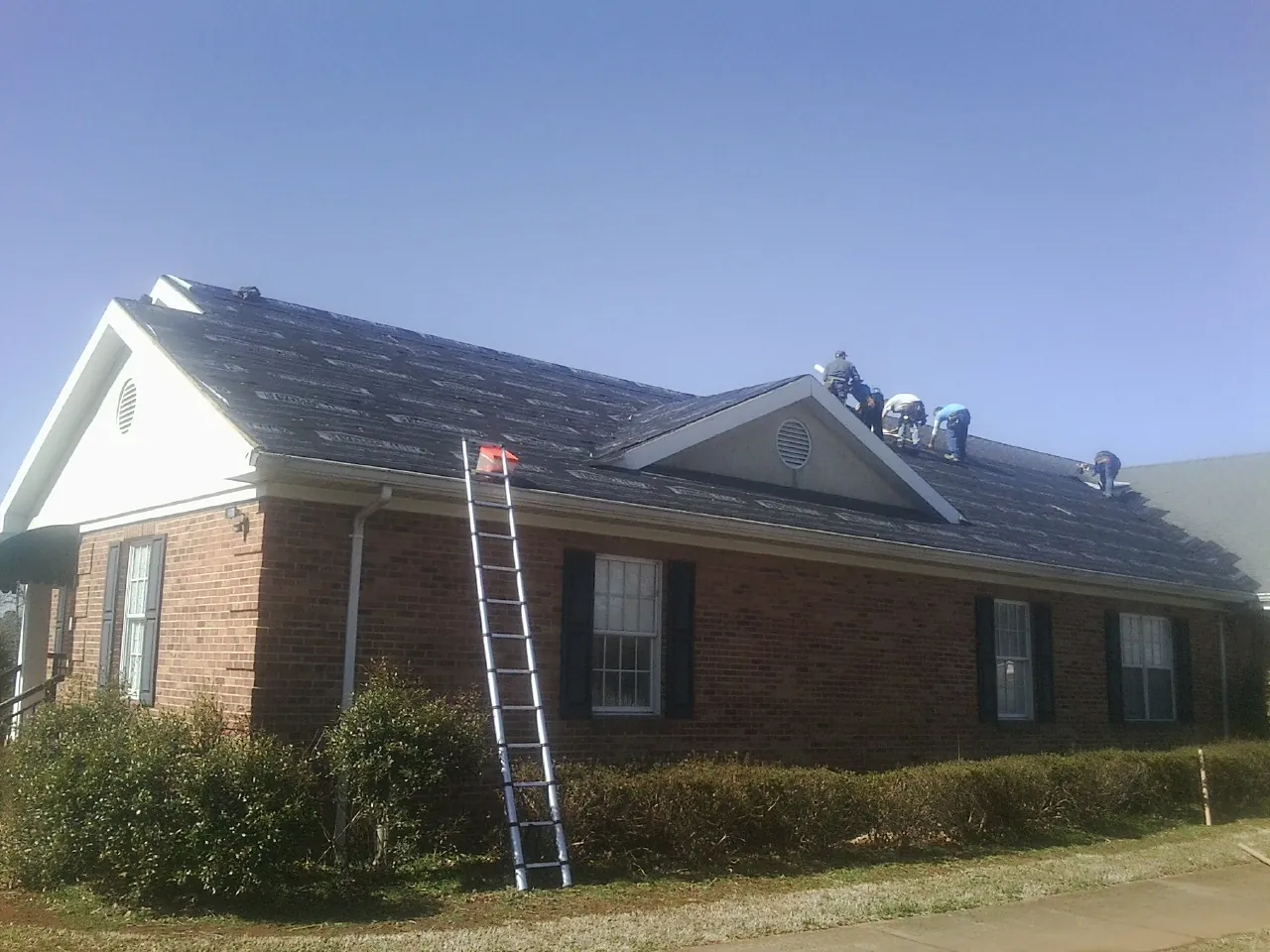 Crew tearing shingles off a brick ranch roof with a ladder set — Metal Roof Repair work by our crew in Casar