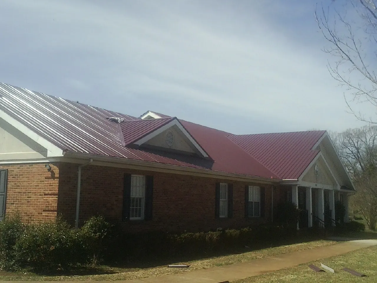 Red metal roof with gabled entries on a long brick building, from a Hail Damage Roof Repair job in Casar