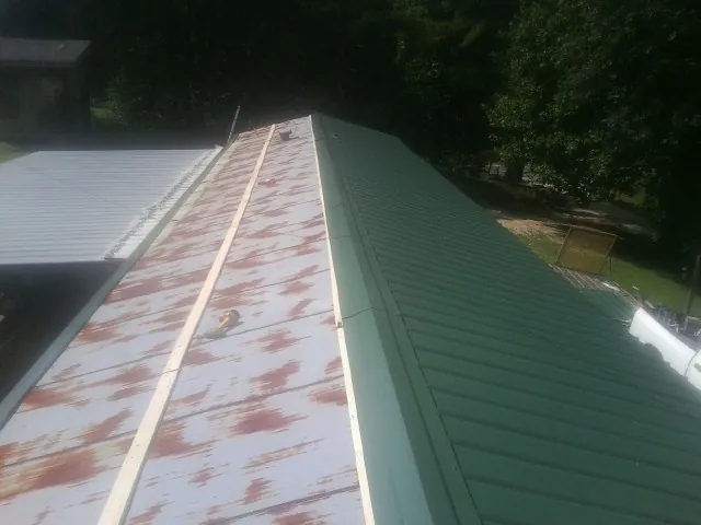 Old rusted panels beside newly installed green metal roofing — Wind Damage Roof Repair by Roofing Brothers in Casar