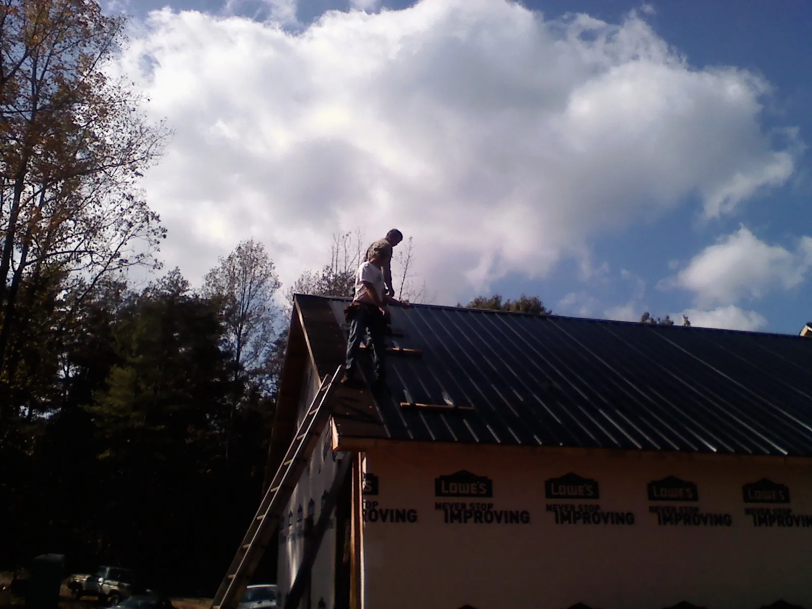 Roofer fastening dark metal panels high against a cloudy sky, from a Roof Inspection job in Casar