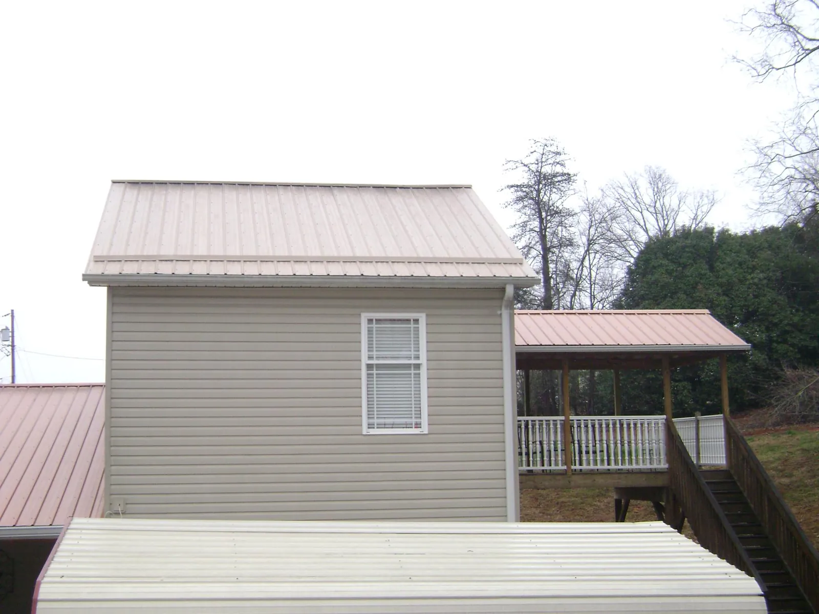 Tan metal roofs on a two story addition and attached porch, from a Roof Replacement job in Casar